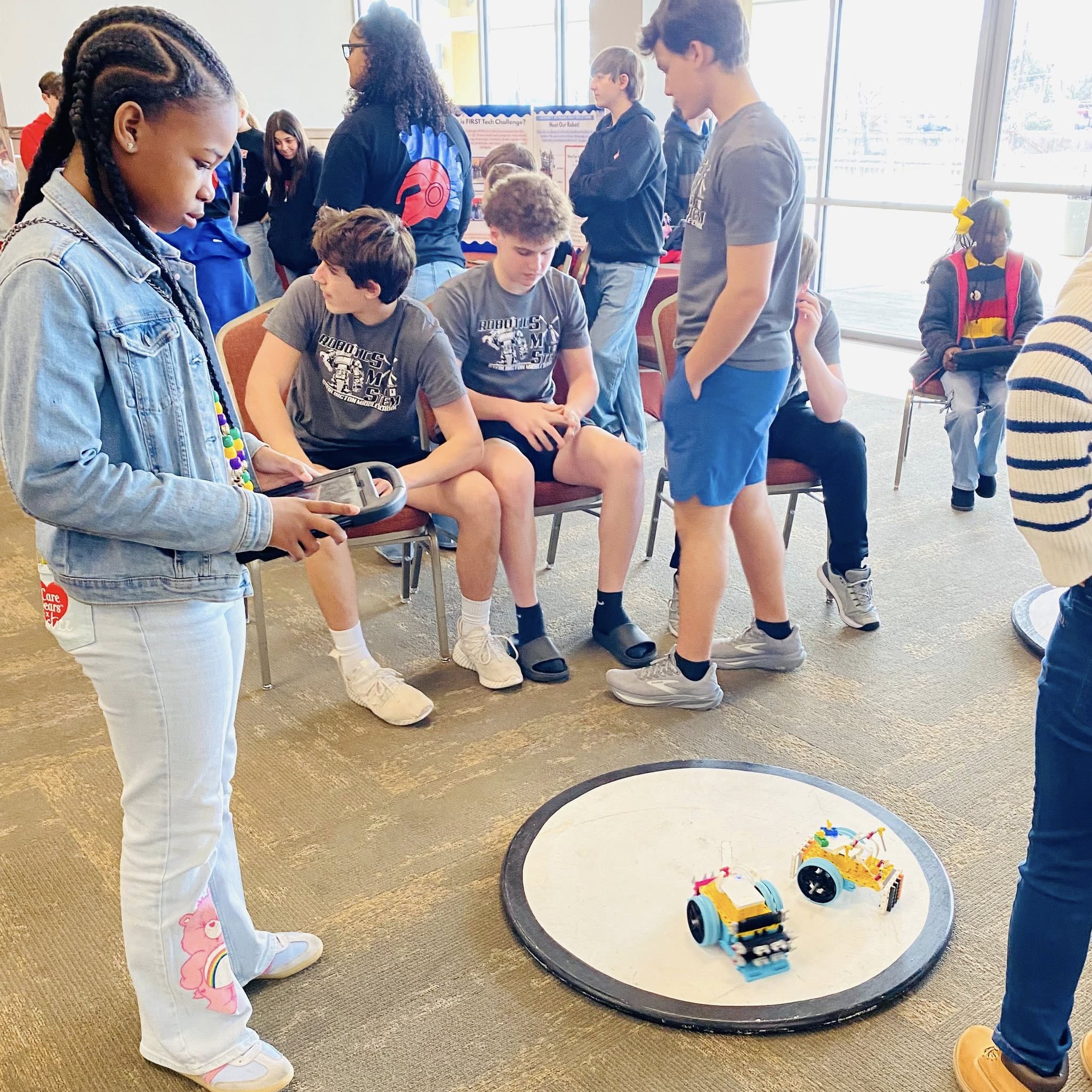 A girl looking at two Lego cars on the floor.